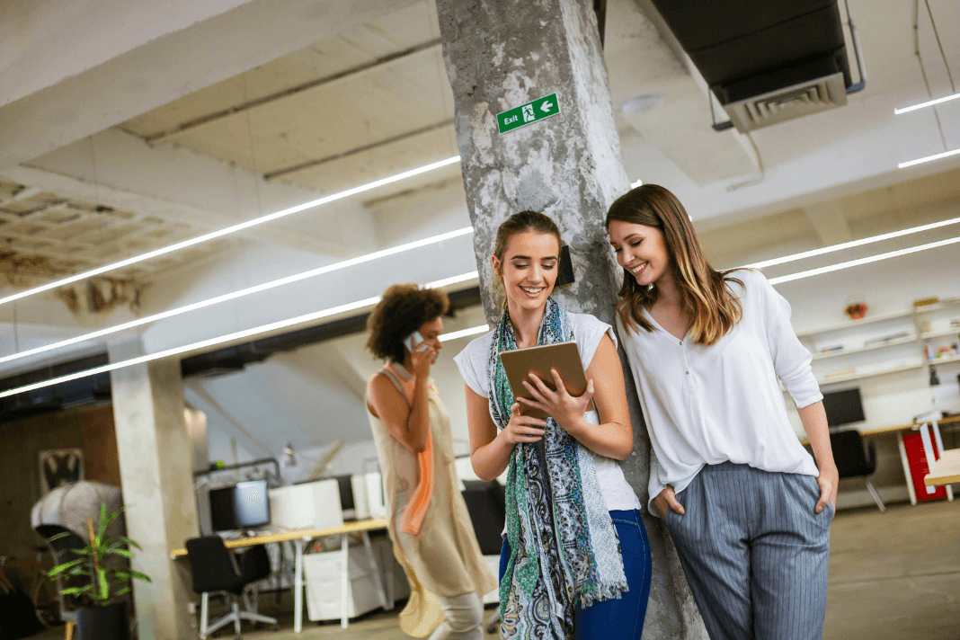 Two women smiling in office looking at iPad