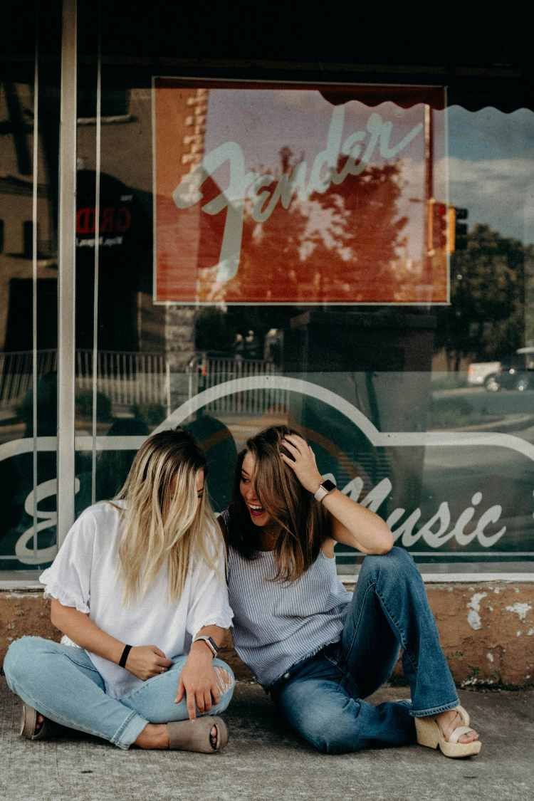 Two young women sitting on the pavement talking